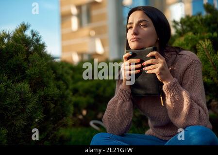 Giovane donna covata e seria che pensa a qualcosa di importante mentre appoggiandosi il mento sul suo diario Foto Stock