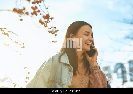 Allegra studentessa è felice e gioiosa chiamata a qualcuno dal suo cellulare all'aperto Foto Stock