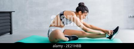giovane donna afroamericana in abbigliamento sportivo che si allunga su tappetino fitness a casa, striscione Foto Stock