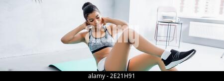 donna afroamericana in abbigliamento sportivo facendo gomito a ginocchio esercizio a casa, banner Foto Stock