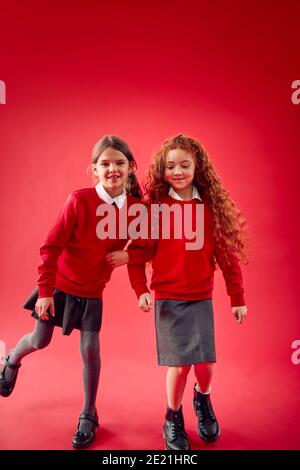 Due allievi della scuola elementare che indossano armi uniformi che collegano contro il rosso Studio sfondo Foto Stock