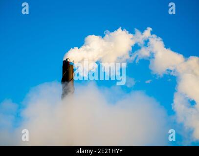 Camino di fumo industriale che mette fuori vapore e fumo su un cielo blu chiaro. Foto Stock