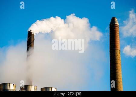 Pile di fumo industriali che emettono vapore e fumo su un cielo blu chiaro. Foto Stock