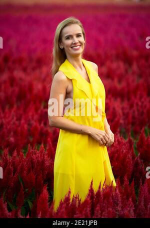 Ritratto di un bel modello in posa in un campo pieno di fiori rossi e viola. Foto Stock
