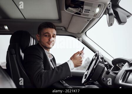 Ritratto di un giovane sorridente che tiene uno smartphone mentre si guida in auto. Affitto e concetto di permuta Foto Stock