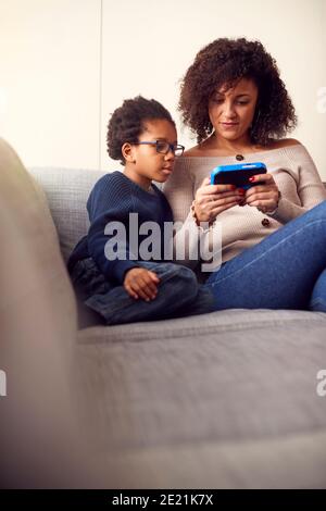 Madre e figlio seduti sul divano a casa giocando computer Gioca insieme su un dispositivo portatile a casa Foto Stock
