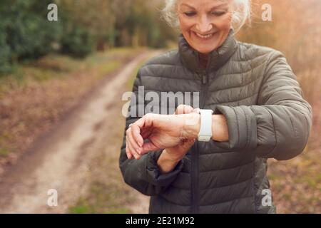 Donna anziana che corre nella campagna autunnale esercitandosi nel controllo dell'orologio intelligente App per attività fitness Foto Stock