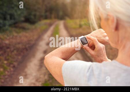 Primo piano di Senior Woman che corre in campagna esercitando controllo App Smart Watch Fitness Activity Foto Stock