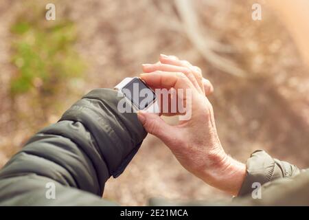 Primo piano di Senior Woman che corre in campagna esercitando controllo App Smart Watch Fitness Activity Foto Stock