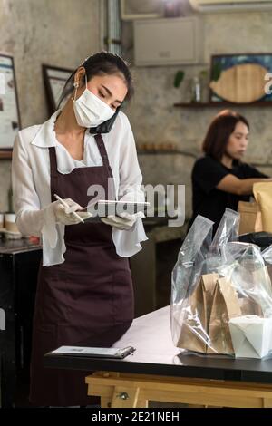 Cameriera asiatica prendere ordine dal telefono cellulare per gli ordini di ritiro e di ritiro dal marciapiede durante il blocco della città. Indossano una maschera protettiva per evitare Foto Stock