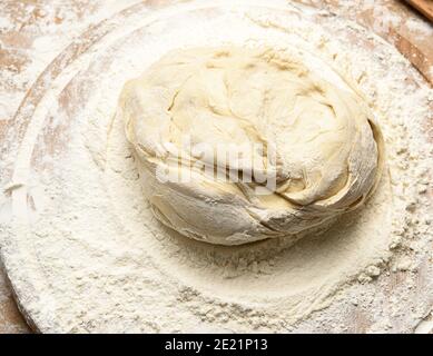 l'impasto impastato di farina di grano bianco giace su un asse di legno rotondo, vista dall'alto Foto Stock