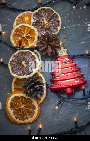 Giocattolo rosso dell'albero di Natale, fette aranciate e luci di ghirlanda su sfondo scuro vintage. Composizione del nuovo anno, messa a fuoco selettiva, sfocatura. Foto Stock