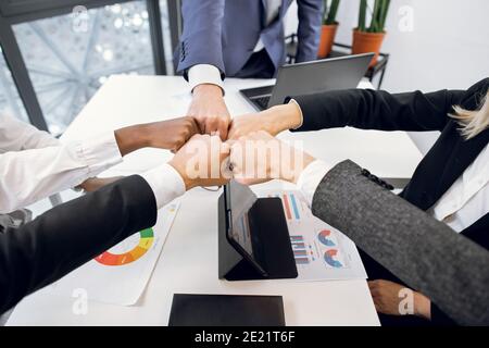 Primo piano vista dall'alto di diverse persone aziendali di etnia, mettendo insieme i pugni sul posto di lavoro, celebrando la riuscita startup, come simbolo di Foto Stock