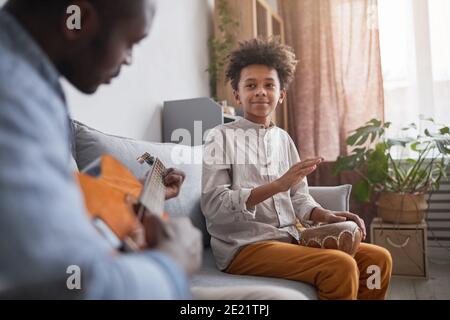 L'uomo afroamericano maturo ed il suo figlio teen che spende grande tempo insieme a casa per suonare musica su chitarra e djembe Foto Stock