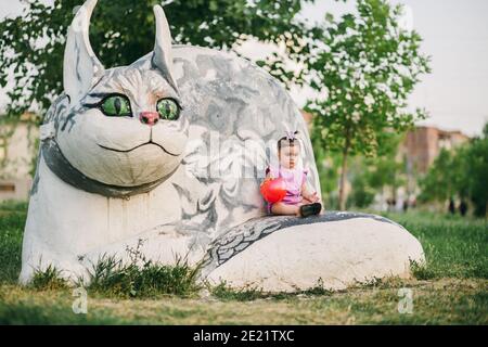 Triste bambino con palla rossa seduta su pietra statua di gatto nel parco Foto Stock