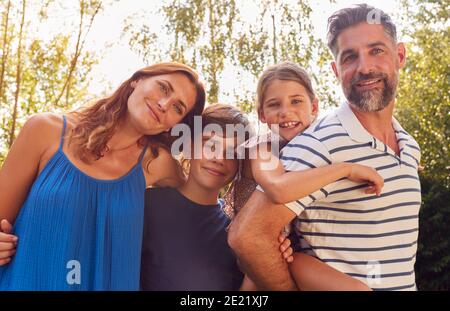 Ritratto di sorridente Famiglia nel Giardino d'Estate con Padre che dà Daughter Piggyback Ride on Back Foto Stock