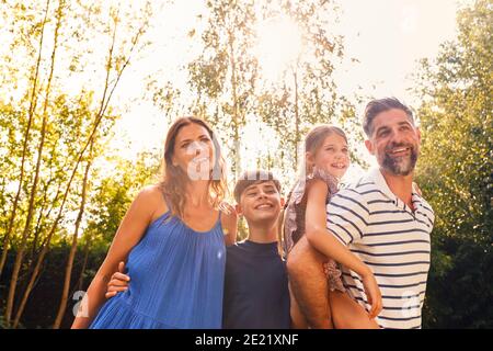 Ritratto di sorridente Famiglia nel Giardino d'Estate con Padre che dà Daughter Piggyback Ride on Back Foto Stock