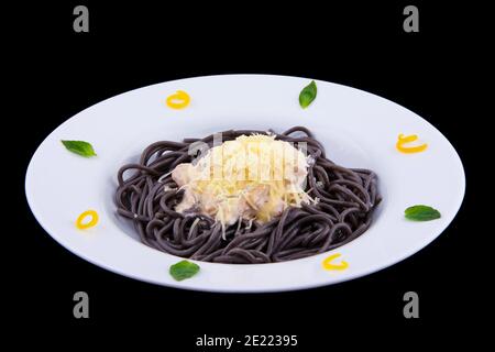 Spaghetti neri con frutti di mare in salsa bianca e formaggio su un piatto bianco su fondo nero. Foto Stock