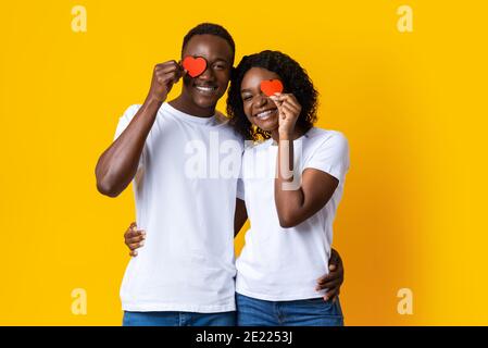 Gli amanti neri abbracciano e tengono i cuori rossi sul giallo Foto Stock