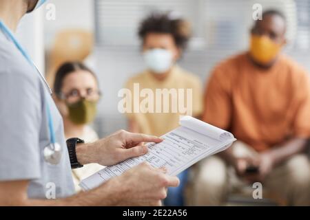 Primo piano del medico di sesso maschile tenendo appunti mentre si parla con i pazienti in attesa in linea presso la clinica medica, copia spazio Foto Stock