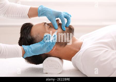 Vista laterale di uomo bearded che ottiene l'iniezione di bellezza alla clinica Foto Stock