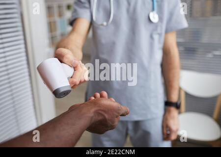 Primo piano del medico maschile che punta termometro a infrarossi alle mani del paziente durante il controllo della temperatura in ospedale, spazio di copia Foto Stock