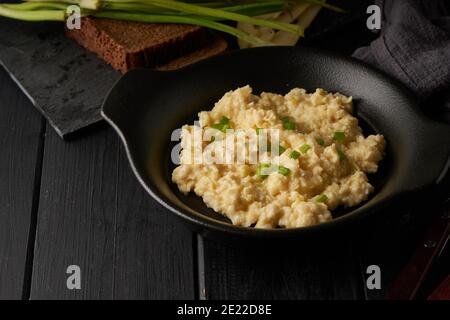 Uova strapazzate con cipolla verde servite in piatto scuro con pane sul tavolo nero Foto Stock