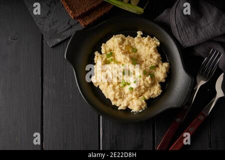 Uova strapazzate con cipolla verde servite in piatto scuro con pane sul tavolo nero Foto Stock