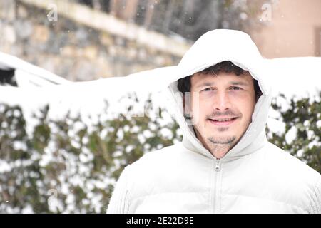 Ritratto di uomo sorridente accanto a cespugli innevati. Vestita con giacca bianca, capelli marroni con capelli grigi. Filomena temporanea. Foto Stock