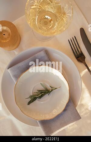 Piatto d'epoca decorato con ramificazione di rosmarino e vetro di crystall con vino bianco Foto Stock