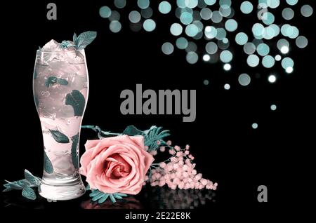 Cocktail con menta e fiori, su sfondo nero con bokeh. Immagine colorata Foto Stock