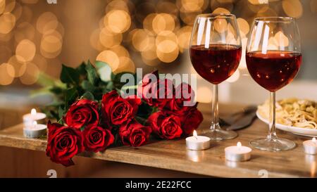 Rose, due bicchieri di vino rosso e candele alla scrivania Foto Stock