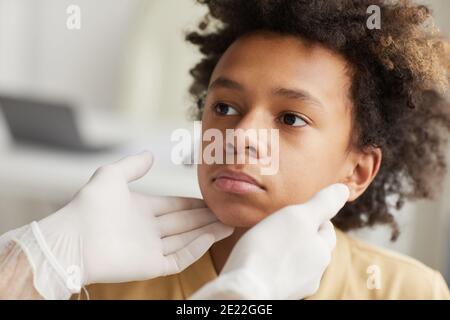 Primo piano ritratto di un medico irriconoscibile che esamina il collo di afroamericano ragazzo durante la consultazione in clinica Foto Stock