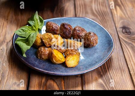 Patate fritte in una uniforme e cotolette di carne in un piatto con verdure su un tavolo di legno marrone Foto Stock