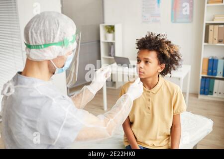 Vista ad angolo alto del medico di sesso maschile che prende il test del tampone di covid Da ragazzo afroamericano in clinica medica Foto Stock