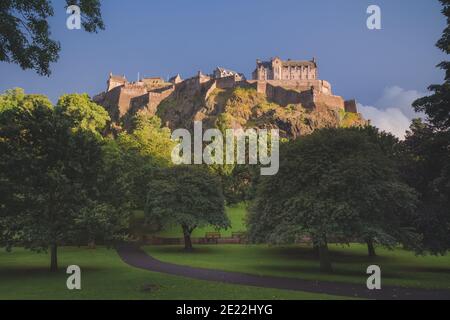 Castello di Edimburgo visto dai giardini di Princes Street la sera d'estate con luce dorata e moody, cielo drammatico. Foto Stock