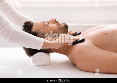Spa terapeuta femminile mettendo pietre nere sulle spalle rilassate dell'uomo Foto Stock