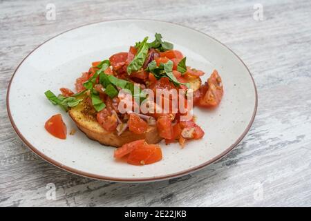 Bruschetta, pane tostato con aglio e olio d'oliva, servito con pomodori a dadini, cipolla e basilico, popolare antipasto italiano su un piatto e una tavola grigia Foto Stock