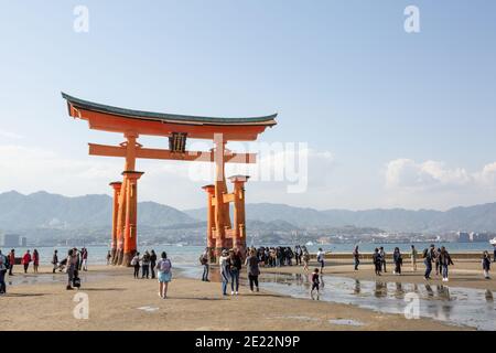 Torii gate, Itsukushima (Miyajima), Giappone, con i turisti a piedi sulla spiaggia. Foto Stock