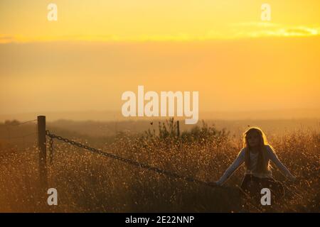 La giovane bionda si siede su una catena in un oro tramonto Foto Stock