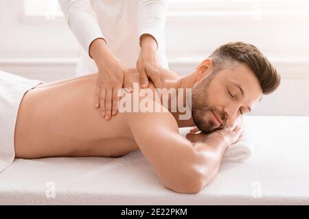 Terapista femminile che sfrega le spalle dell'uomo gioioso al salone termale Foto Stock