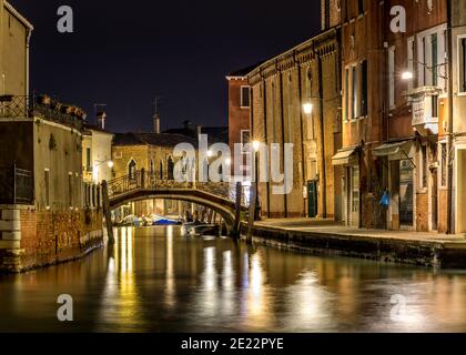 Notte a Murano - Vista notturna di un piccolo ponte di mattoni, Ponte San Pietro Martire, che attraversa uno stretto corso d'acqua, al centro di Murano, Italia. Foto Stock