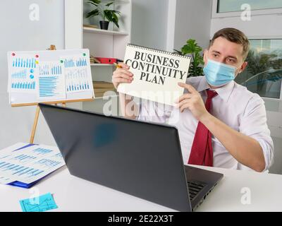 Man in face mask mostra il piano di Business Continuity durante la riunione online. Foto Stock