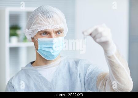 Ritratto di infermiere di sesso maschile indossando la maschera e l'attrezzatura protettiva che tiene la fiala con la medicina mentre si lavora in clinica o in ospedale, copia spazio Foto Stock