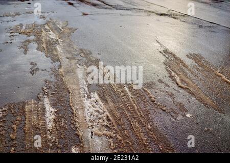 Tracce di pneumatici nella neve che scioglie su strada asfaltata. Messa a fuoco selettiva morbida Foto Stock