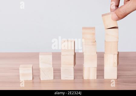Mano che mette e accatastando i cubi di legno vergini sul tavolo con lo spazio di copia. Disposizione manuale di blocco di legno impilato come scala a gradini. Concetto aziendale. Foto Stock