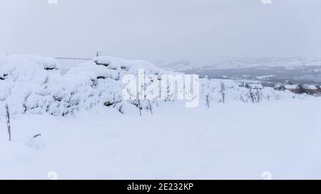 Campagna inglese paesaggio innevato immagine di un muro di pietra secca coperto di neve che conduce in un villaggio inglese in Lancashire, Inghilterra. Foto Stock