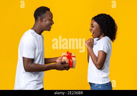 Amorevole uomo afroamericano che dà presente alla sua moglie eccitata Foto Stock