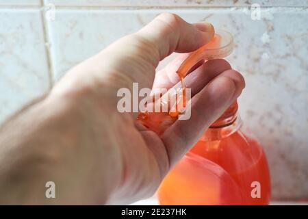 Chiusura della mano maschio con sapone liquido, pressione della pompa dell'erogatore con il pollice e applicazione del flusso di sapone sul palmo. Concetto di igiene personale. Foto Stock