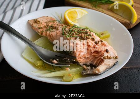 Salmone in camicia con finocchio e limone: Un pezzo di salmone erbaciato su finocchio bollito cotto in brodo di limone Foto Stock